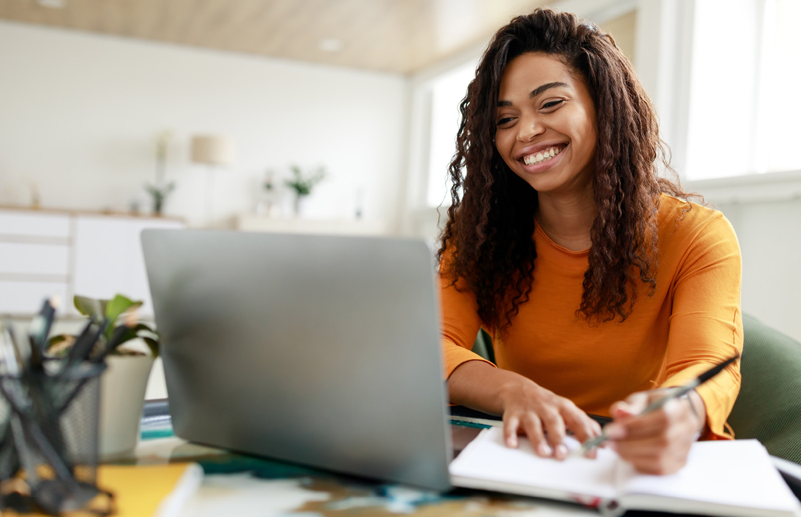 Professional learner smiling while working on a laptop and taking notes.